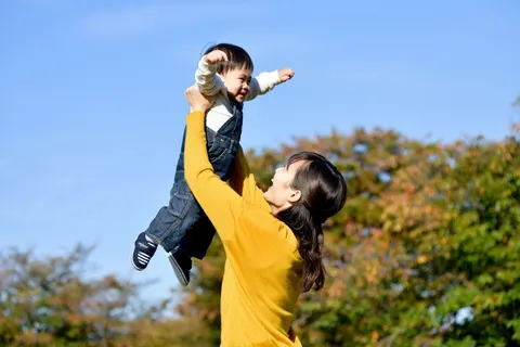 晴れた屋外で、子どもを両手で持ち上げてあやす女性